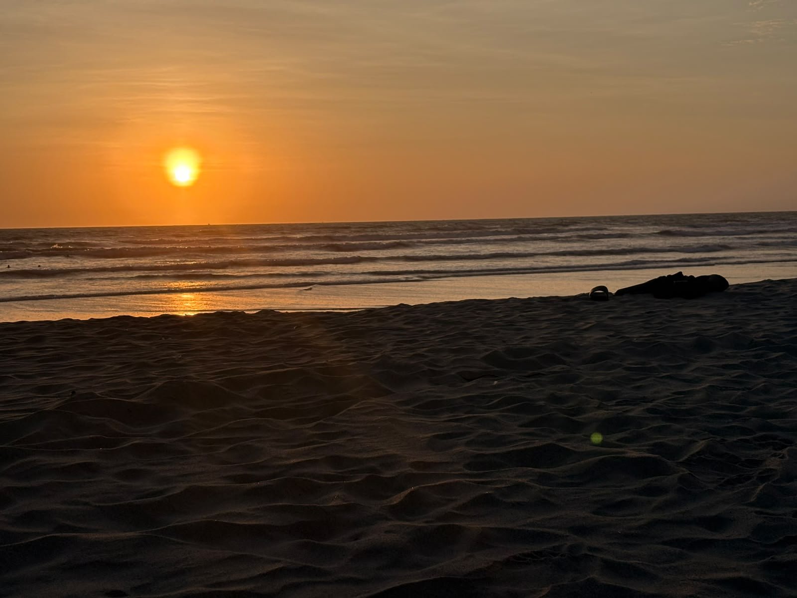 El sol bajando sobre el mar, con la arena en primer plano